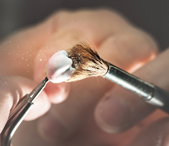 An up-close image of a person’s finger and a customized dental crown resting on top of it