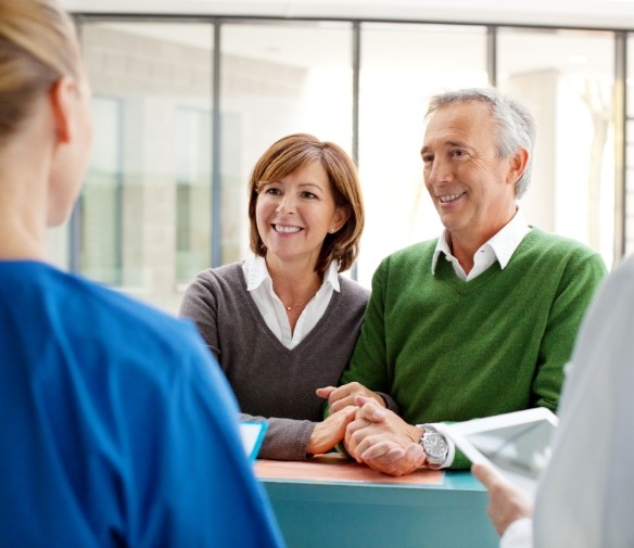 Man and woman checking in at reception desk for dental implant tooth replacement