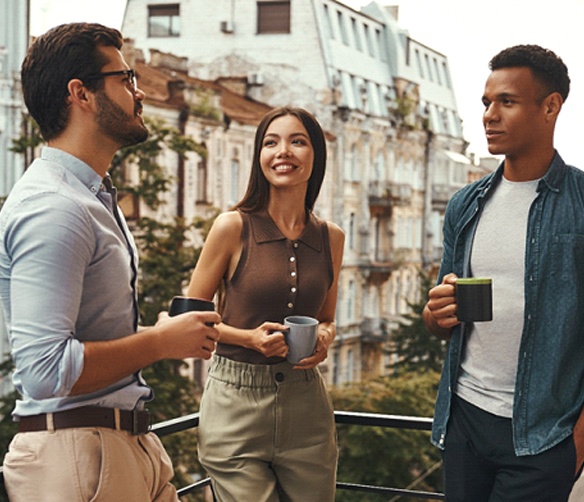 friends talking to each other on a balcony with coffee mugs in their hands